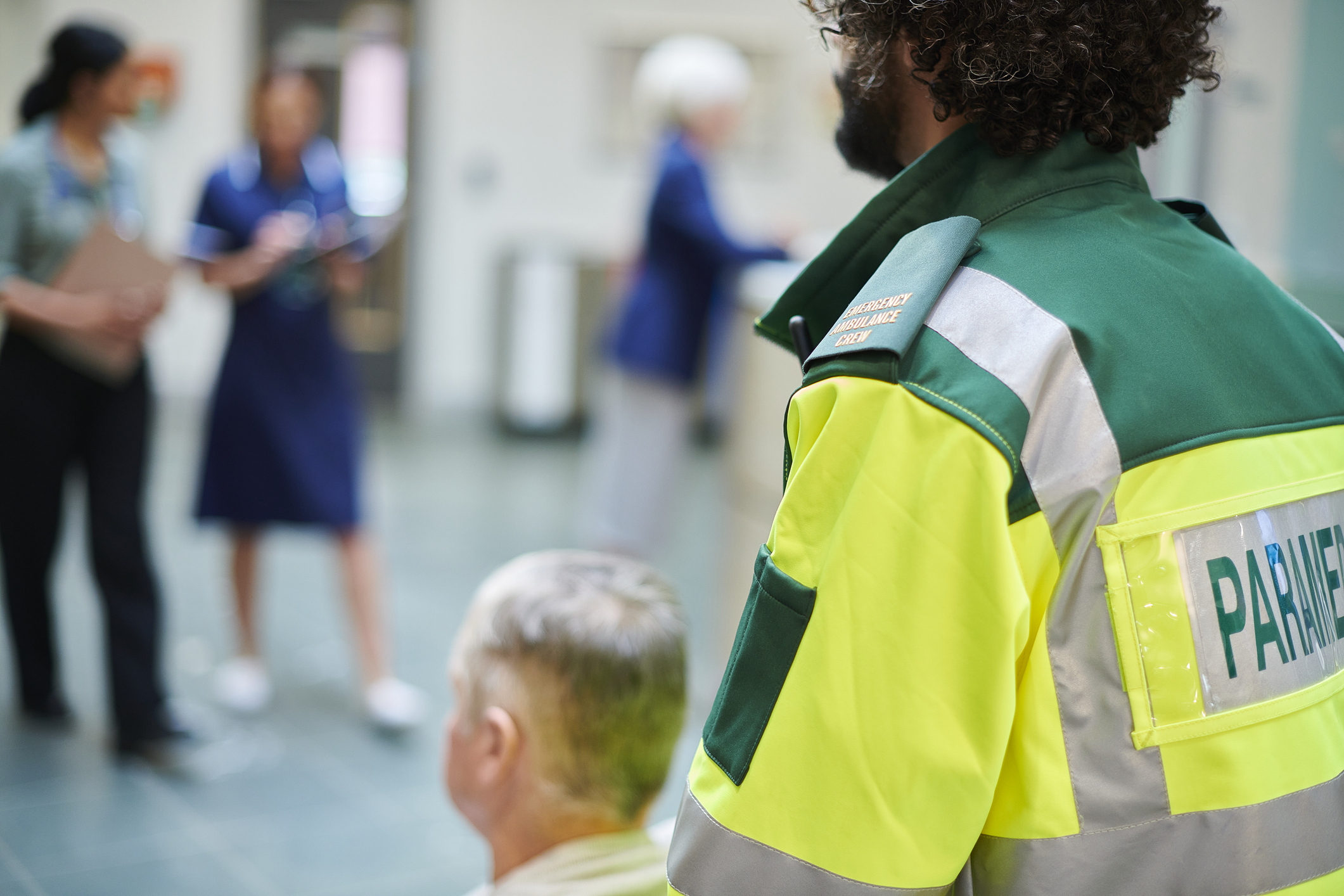 Paramedic bringing patient to hospital in a wheel chair through a busy lobby